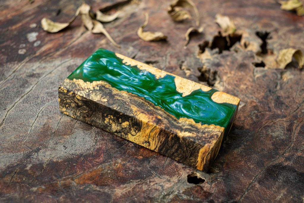 Casting green epoxy resin burl wood cube on old table art backgr